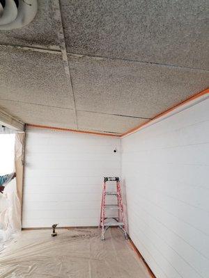 Dirty spray on popcorn ceiling applied to plywood surfaces. Removed the plywood and installed new drywall, lighting and texture.