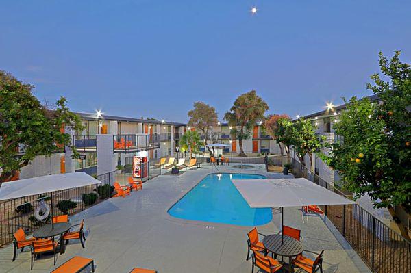 Sparkling Swimming Pool at Dusk surrounded by Orange chairs and tables with umbrellas