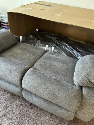 A partial put together grey reclining loveseat half outside the box