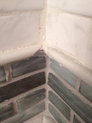 Tile strip in middle of shower wall that includes cracked tiles and pieces that don't meet.