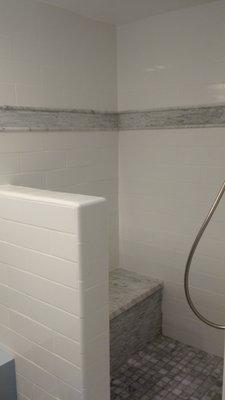 Shower with artic white subway tiles pony walls and walls with Carrara marble accent, bench, floor and shelves.