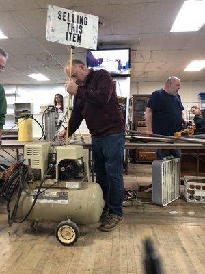 Rick, owner of Heatwole Auction Team, displying item for sale while faithfull employees Art & Peanut look on.