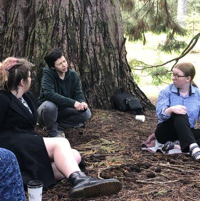 a conversation at one of our Big Tree Gatherings: 3 young adults sit beneath a Sequoia, listening intently