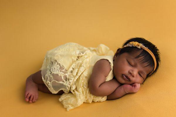 newborn photoshoot baby girl posed on yellow backdrop