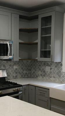 Light gray shaker cabinets, quartz countertops, custom made exposed shelves and gray ceramic for backsplash.