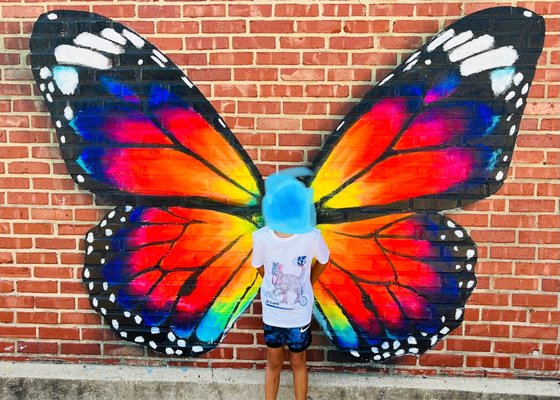 My son taking a photo in front of butterfly mural outside.