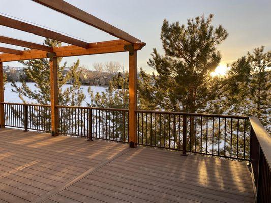 A sunset picture of a composite deck. The deck has Deckorators ALX Contemporay Brown railing with a drink rail (deck board) m...