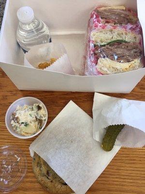 Pastrami sandwich with pickle, cookie, water, potato salad and chips