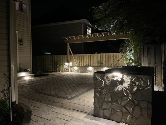 Island with built-in grill and cooktop. Paver patio. seating wall with trellis. Hardscape and Landscape lighting.