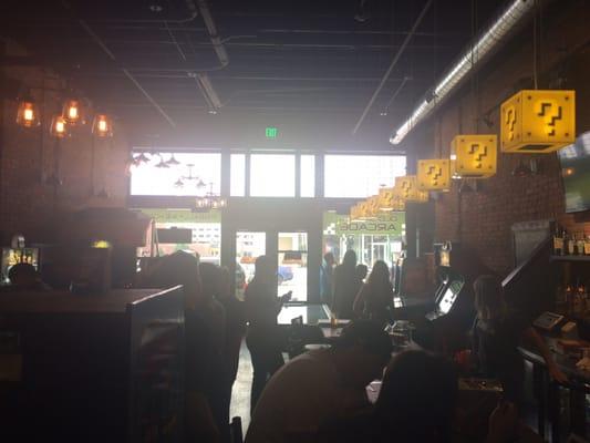 An intimate space with "Mario" lights above the bar top. Air hockey in the middle and arcade and pinball machines along the wall.