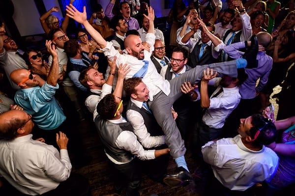 Groom is lifted into the air by wedding guests during wedding reception.