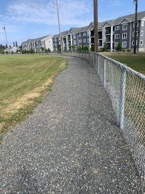 Gravel walking path along the outside of the baseball fields by the fence.