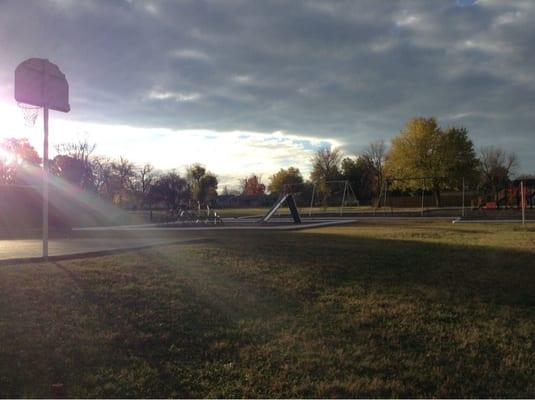 One view of playground which includes jungle gym, swings, dome, slide, track, & basketball court. (And is fenced in)