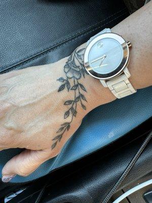 Delicate wrist/hand tattoo of flowering leaves.