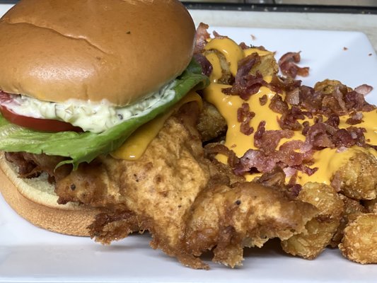 Fish sandwich topped with tartar, lettuce and tomato. With loaded tater tots...