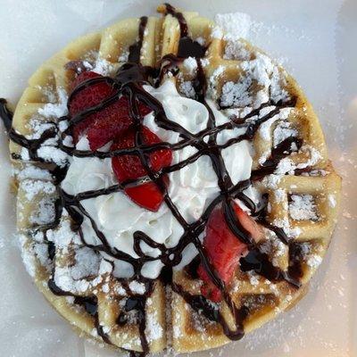 Strawberry waffle topped with fresh strawberries, whipped cream and chocolate drizzle