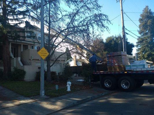 truck with conveyor used to load roofing shingles directly to top of next door 3 story house