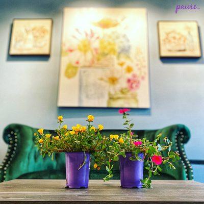 Two flowering plants in front of a green couch and artwork on the walls