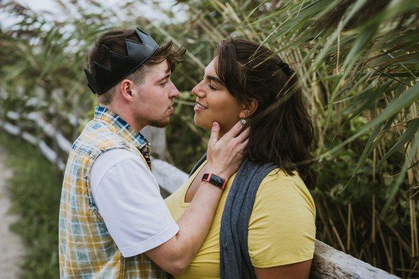 Vince and Richa hold each other by the beach, surrounded by tall grasses