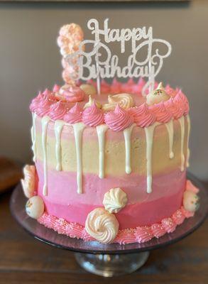 Beauty in pink!  Lovely white cake with a light ombré buttercream frosting. Topped with a white chocolate drip and meringue kisses.