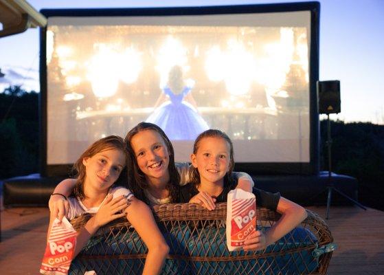 Teenagers having an outdoor movie screen rental in their backyard while eating tasty popcorn.