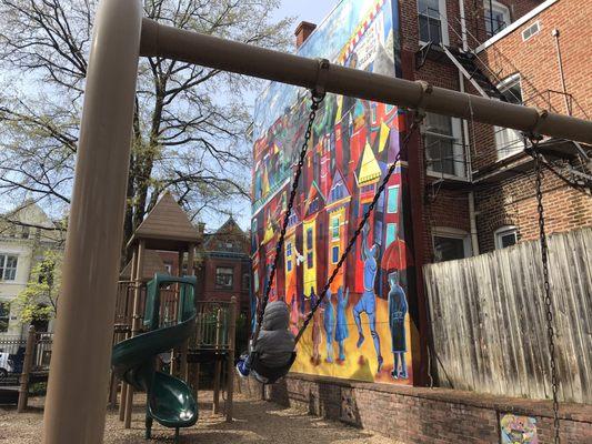 Swingset with larger play structure in front of a beautiful mural