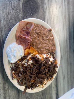 Chilaquiles with fajita on top with sour cream on the side