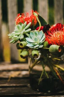 Centerpieces with pin-cushion proteas, ranunculas, sucuulents, keeping our coral red and mint green wedding colors:)