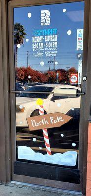 The front door of New Life Thrift. Hours: M-Sat 9am-5pm. Sun closed. "Thank you for your support". North pole sign image.