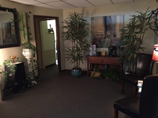 View from entrance into the waiting room. Many live plants, eclectic decor, keurig, and reading materials.