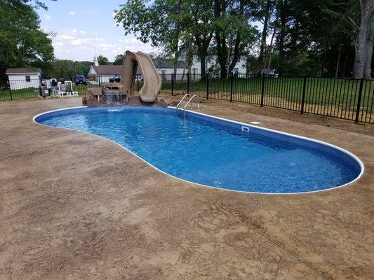 Pool w/ tan ledge, bench , Rico Rock waterfall and slide.
 Stamped/colored concrete, fencing. Work completed by Amazing Walls and Waterfalls