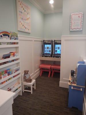 Kids waiting area equipped with arcade games, books, and a play kitchen