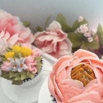 Pink buttercream floral cupcake with intricate petal detailing, accompanied by a second flower in yellow and green.