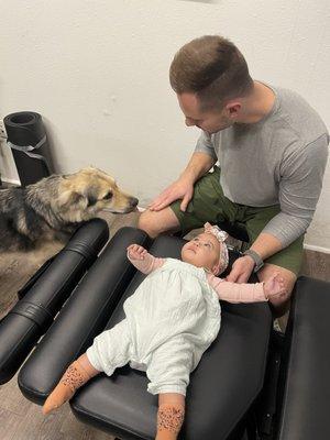 Dr. Chris Jepsen working with an infant while the office dog Koa helps out.