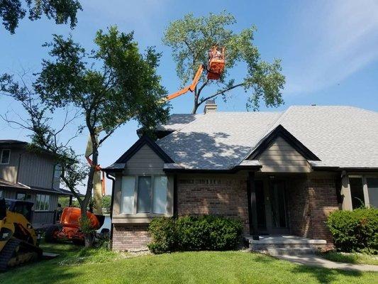 Crews using a high-reach aerial platform to remove a tree over the roof.