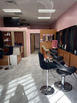 his photo shows the interior of a hair salon with a modern and minimalistic design. The room has pink walls and a white marble-like floor.