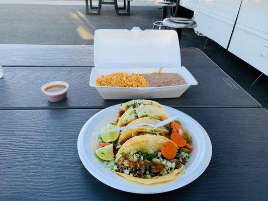 Refried beans, rice, spicy pork taco, beef steak taco, shredded chicken taco and fried pork taco with a side of hot sauce.