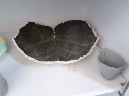 Clay project with a large leaf impression drying to be bisqued.