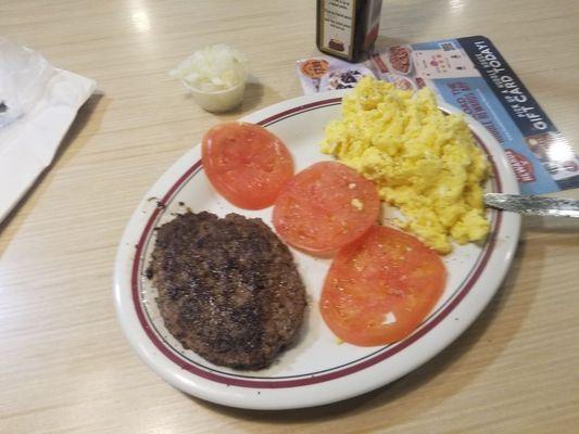 Hamburger steak, scrambled eggs, and sliced .