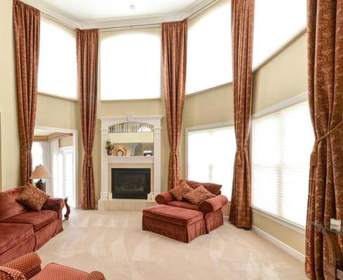 A gorgeous 2-story family room with floor to ceiling drapes and Motorized Duette Honeycomb Shades.