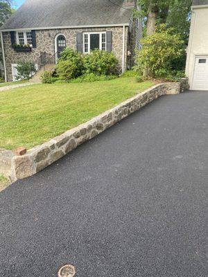 Low Natural stone retaining wall and asphalt driveway.