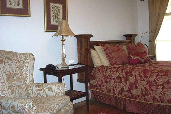 This Veranda Room features hardwood floors, dark wood furniture, a comfy chair, and a queen size bed.