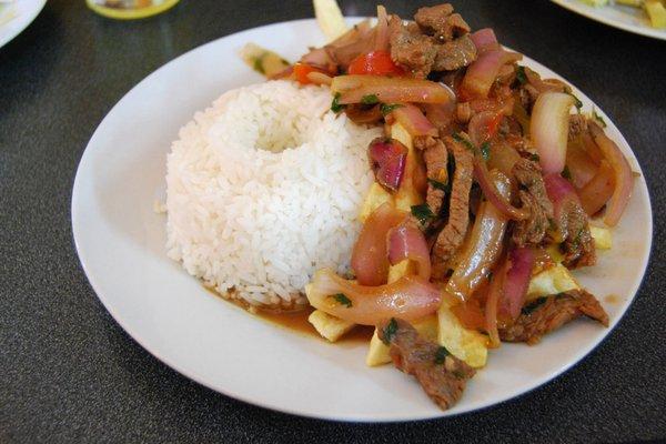 Lomo Saltado.  Strips of delicious steak with pepers , onions, tomatoes and french fries served with white rice and green hot sauce/aji.