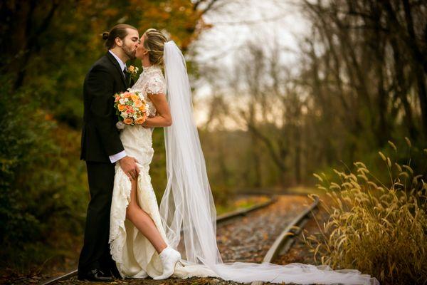 Bride and groom kissing along railroad tracks in the woods. Photography by Phil Kramer