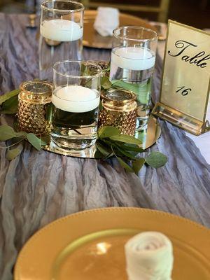 Floating candles with gold votive holders on mirrors and greenery