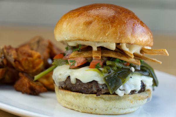 Poblano Burger: All-beef patty topped with cheese, roasted poblano chilis, pico de gallo, fried corn chips, and aioli on a
toasted bun.