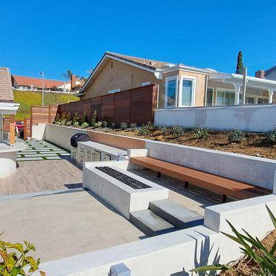 Smooth finished stucco wall, outdoor kitchen, sitting bar, fire pit. Flooring is porcelain tile and custom mangaris wood benches and fence.