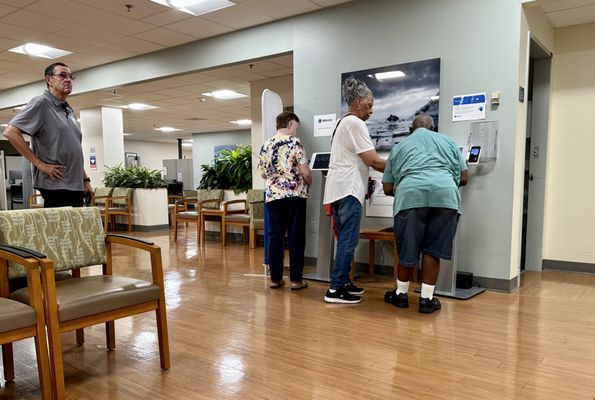 Elderly patients line up to check in on a 15 page machine. Good luck if you don't have your glasses!