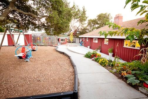 Huge outdoor space with play structure and swings to the left, a bike path and a separate sand box and play area around the corner.