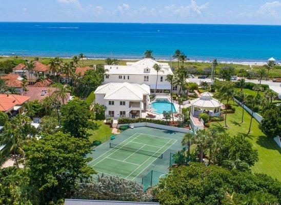 A tennis court and a large house with a pool in the background